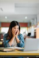 A young woman in a casual setting expresses surprise while using a laptop, surrounded by books in a cozy cafe environment. photo