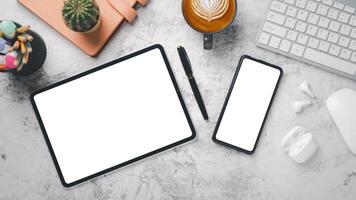 Office desk workplace with blank screen tablet and smartphone, keyboard, mouse, notebook, pen and cup of coffee, Top view flat lay. photo