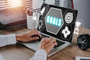 Goals concept, Businessman using laptop computer on office desk with goals icon on virtual screen. photo