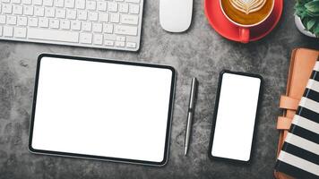 Office desk workplace with blank screen smartphone and tablet, pen, keyboard, mouse, notebook and cup of coffee, Top view flat lay. photo