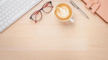 Office wooden desk workplace with keyboard computer, notebook, pen, eyeglass and cup of coffee, Top view flat lay with copy space. photo
