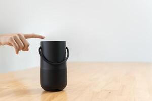 Close-up of hand pressing a button on a wireless Bluetooth speaker surrounded by blurred background. photo