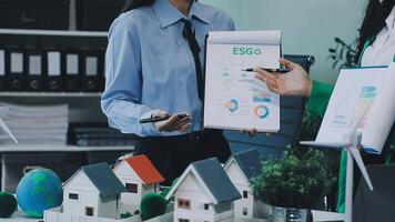 Two people are standing in front of a desk with a house and a model video