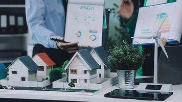 A man is working on a project with a model of a house and a wind turbine video