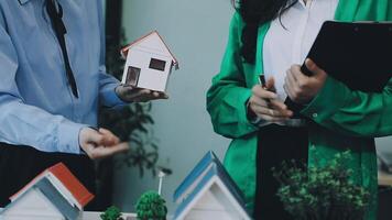 Two people holding a house model and a clipboard video