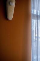 a wall of rich beige color with a lamp. next to a large window. the lamp is oval, it hangs on the wall with ceramic elements. photo
