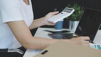 A woman is using a calculator to calculate the cost of a laptop video