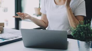 A woman is sitting at a desk with a laptop and a phone video