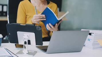 A woman is sitting at a desk with a laptop and a notebook video