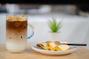 Side view of ice latte coffee with butter cake in a glass on wooden table photo