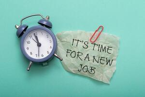 A clock is on a table with a piece of paper that says It's time for a new job photo