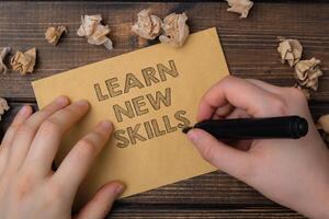 A person is writing on a piece of paper that says learn new skills photo