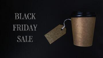 Coffee cup with a gold tag on it is on a black background with the words Black photo