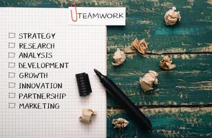 Piece of paper with a black marker on it with the word teamwork written in red photo