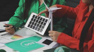 Two people working on a laptop with a wind turbine video