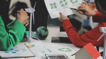 Two people working on a project with paper and a wind turbine video