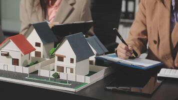A woman is writing on a piece of paper while looking at a model of a house video