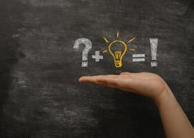 Hand is holding a chalkboard with a question mark, plus sign, and light bulb photo