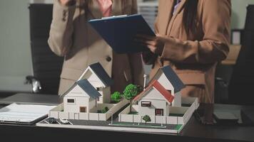 Two business people standing in front of a model house video