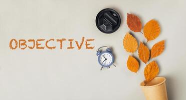 Clock and a cup are on a table with the word objective written in orange photo