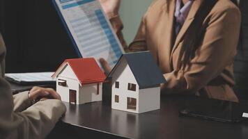 A woman is holding a house model and a man is looking at it video