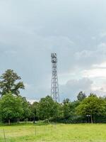 Tall tower with a cell phone antenna on top stands in a field photo