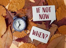 Clock is on a pile of leaves with the words if not now when photo