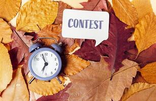 Clock is on top of a pile of leaves with the word Contest written in a speech photo