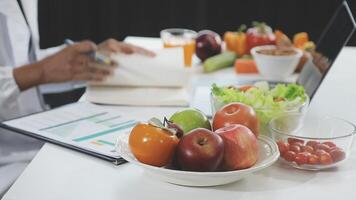 A doctor is working on a laptop while sitting at a table with a bowl of fruit and vegetables video