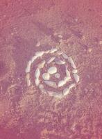 Shells laid out in a spiral lie on the sand. twisted spiral from seashells on the beach, gently pink tinting. round shape from small shells. the photo has a vertical orientation