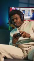 vertical africano americano homem tocam intenso conectados jogos às lar, spamming ataque botões em dele controlador. jogador participando dentro conectados concorrência, jogando em jogos console. Câmera b. video