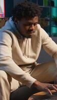 Vertical African american male freelancer managing creative projects remotely in his loft, working on a new novel or script for his gig. Man focusing on writing and editing creation, telework. Camera B. video