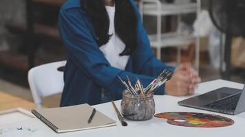 A woman sitting at a table with a laptop and paintbrush video