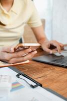 Close-up of a person multitasking with a smartphone and laptop at a desk, surrounded by charts and documents. photo