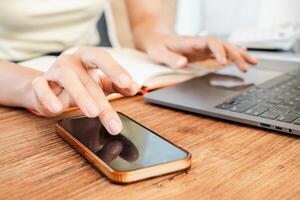 Hands interacting with smartphone and laptop on a wooden desk, illustrating multitasking and remote work in a modern office setting. photo