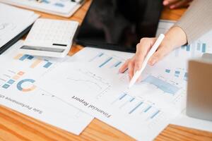 Close-up of a person reviewing financial documents with charts, graphs, calculator, and tablet on a wooden desk. photo