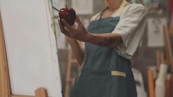 A woman holding an apple in front of an easel video