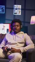 Vertical Bored guy plays online game and spamming attack buttons on his controller, modern loft apartment. Gamer in neon lit space participating in internet e sports competition. Camera B. video
