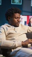 Vertical Black man does his research by reading articles and taking notes at home, collecting information for a new project. Freelancer multitasking and studying files with data driven papers. Camera B. video