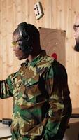 Vertical Portrait of happy army soldiers in shooting gallery looking at targets, comparing points obtained. Cheerful military units testing accuracy in firing range, looking at shot bullseye, camera A video