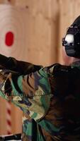 Vertical Portrait of smiling woman in firing range shooting with pistol, wearing earmuffs to protect hearing. Cheerful person in shooting gallery using safety gear to prevent damage from gunshots, camera B video