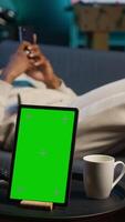 Vertical African american young adult laying on the sofa next to mockup copy space, relaxing and browsing web on his smartphone. Happy relaxed person on the couch feels happy with remote job. Camera A. video