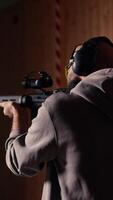 Vertical Man in firing range doing shooting activity with rifle, wearing earmuffs to protect hearing. Person training with semiautomatic weapon, using safety gear to prevent damage from gunshots, camera A video