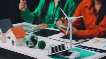 Two women are sitting at a table with a wind turbine and a house video