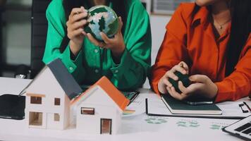 Two women sitting at a table with a model of a house and a globe video