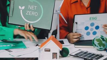 Two people sitting at a table with a laptop and a net zero sign video