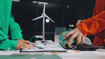 Two people working on a project at a table with a wind turbine video