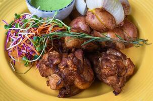 Peruvian Chicken with Green Sauce and salad with potato on a yellow plate close up side view photo