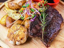 Beefsteak served with potatoes, vegetable and sauce on wooden cut board close up side view photo