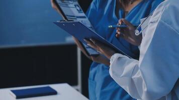 Two doctors are holding a clipboard and looking at a computer video